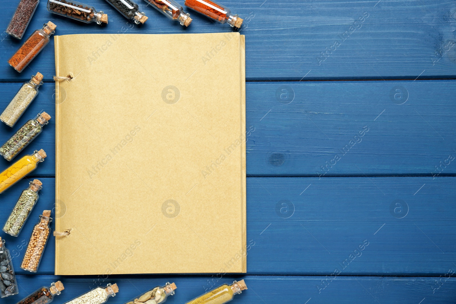 Photo of Blank recipe book and bottles with different spices on blue wooden table, flat lay. Space for text