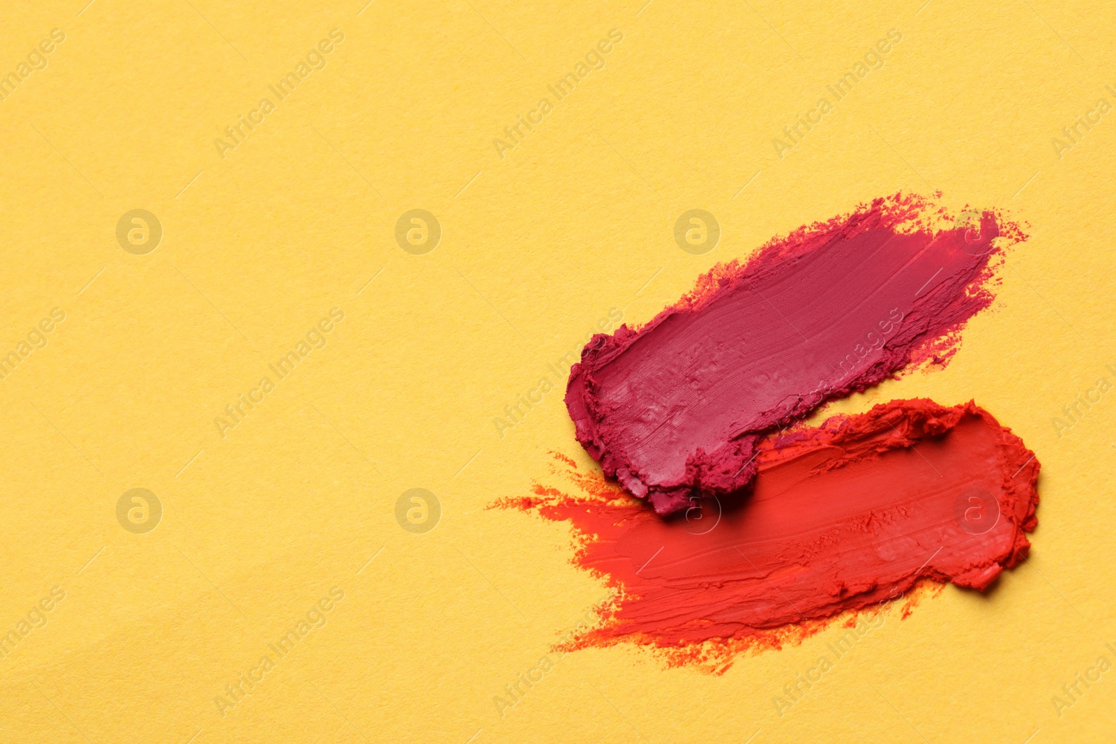 Photo of Smears of bright lipsticks on yellow background, top view. Space for text