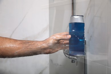 Photo of Man taking bottle of gel from shelf in shower at home, closeup