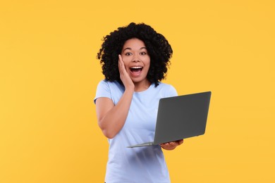 Emotional young woman with laptop on yellow background