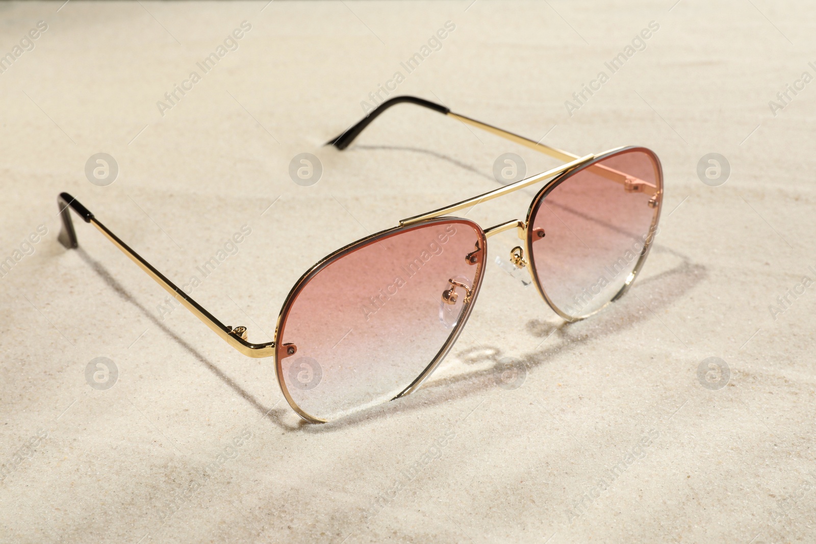 Photo of New stylish sunglasses on sand. Fashionable accessory