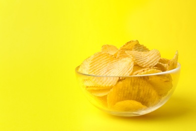 Delicious crispy potato chips in bowl on color background, space for text