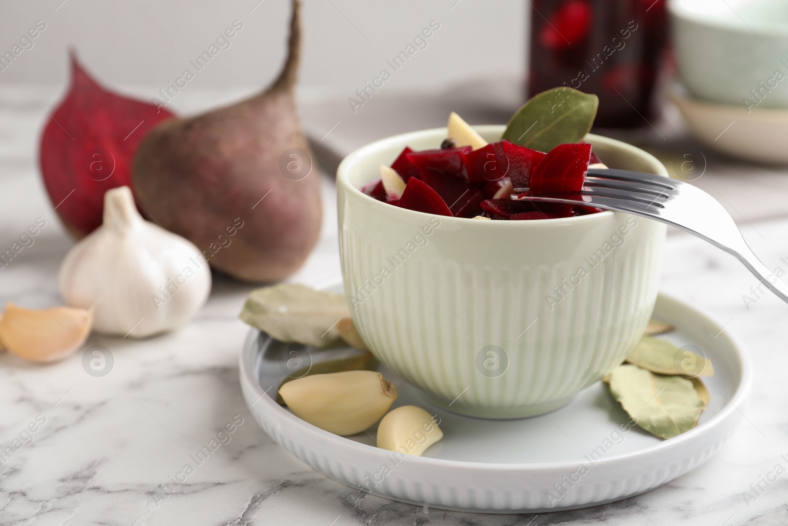 Photo of Pickled beets with garlic in bowl on white marble table