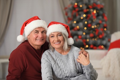 Photo of Happy mature couple in Santa hats at home. Christmas celebration