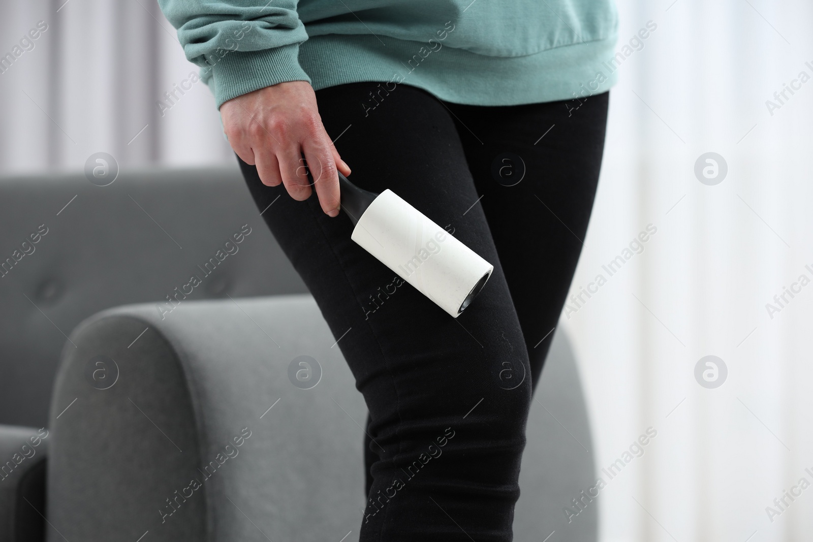 Photo of Woman with lint roller removing pet hair from black trousers indoors, closeup