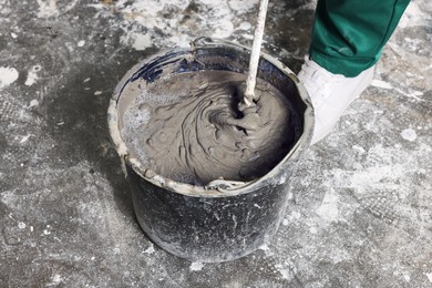 Photo of Worker mixing concrete in bucket indoors, closeup