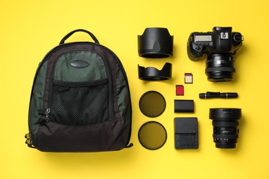 Photo of Backpack, camera and professional photographer's equipment on yellow background, flat lay
