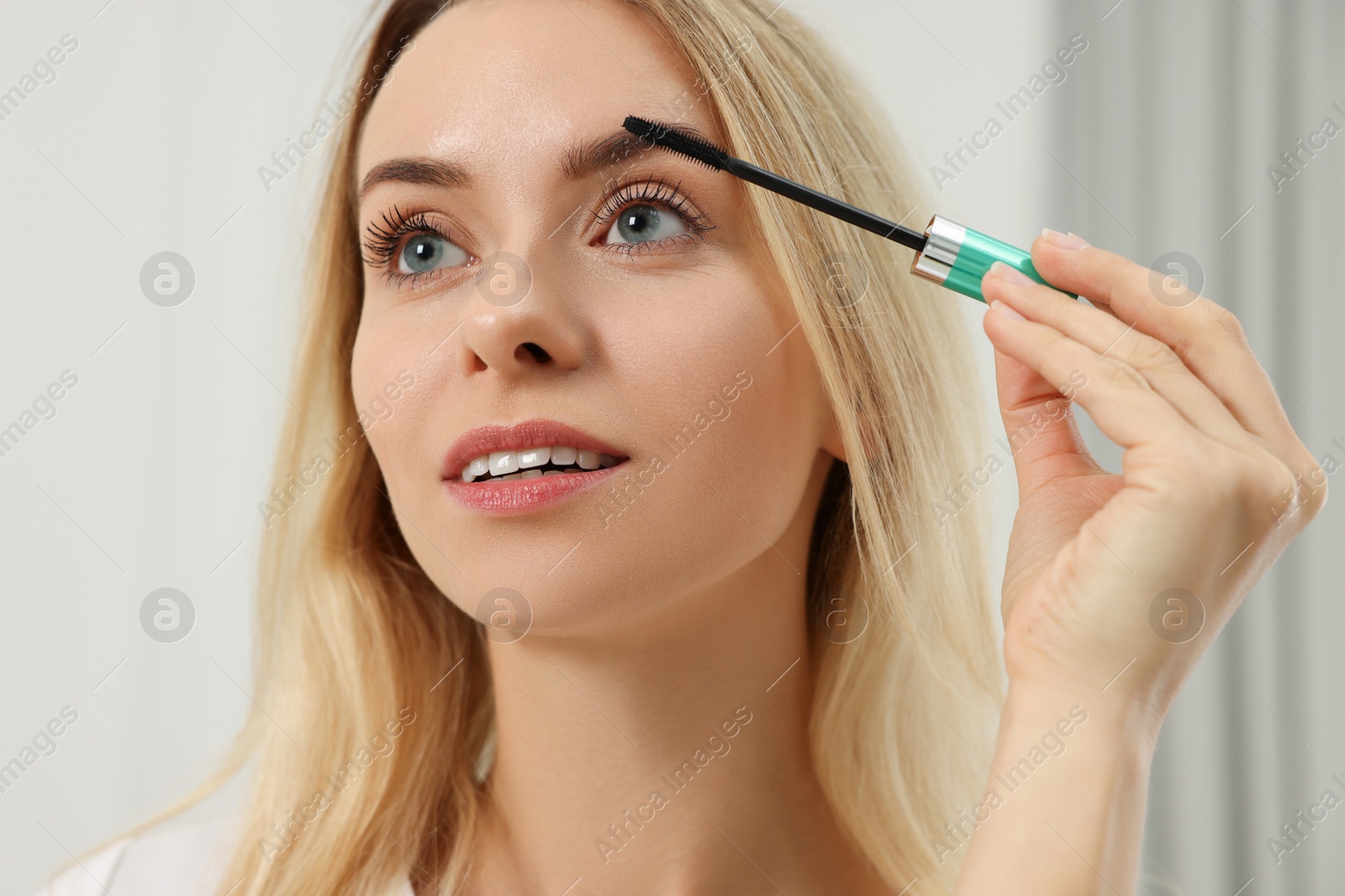 Photo of Beautiful woman applying mascara with brush indoors, closeup