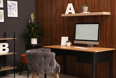 Photo of Comfortable workplace with computer near wooden wall in stylish room interior. Home office design