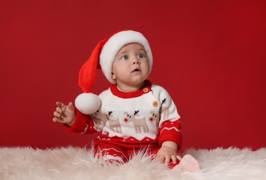 Photo of Cute baby in Santa hat on fluffy carpet against red background. Christmas celebration