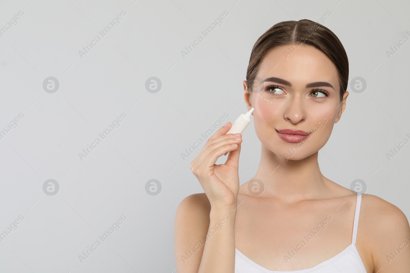 Photo of Young woman applying cream under eyes on white background, space for text