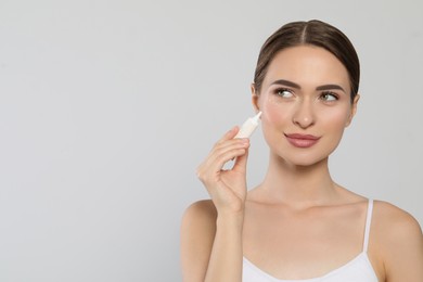 Young woman applying cream under eyes on white background, space for text