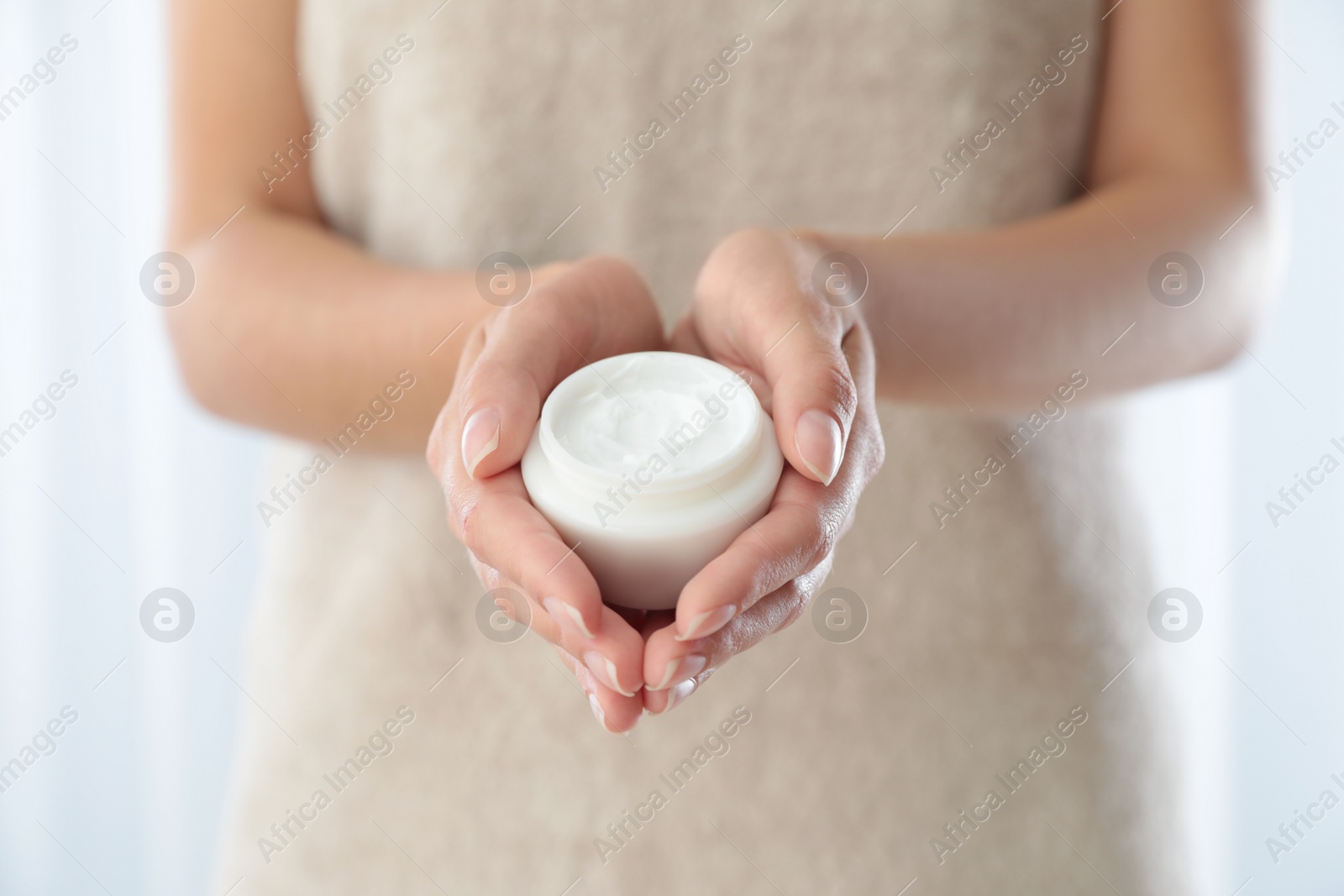 Photo of Young woman holding jar of cream at home, closeup