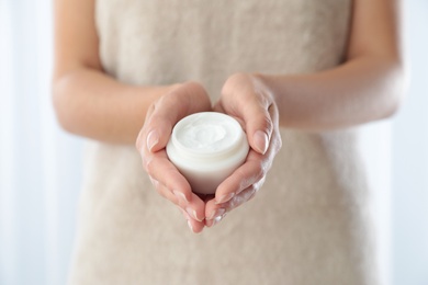 Young woman holding jar of cream at home, closeup