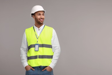 Engineer with hard hat and badge on grey background, space for text