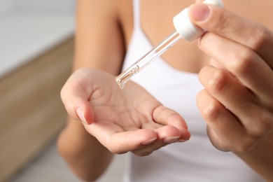 Photo of Woman applying cosmetic serum onto her hand on blurred background, closeup