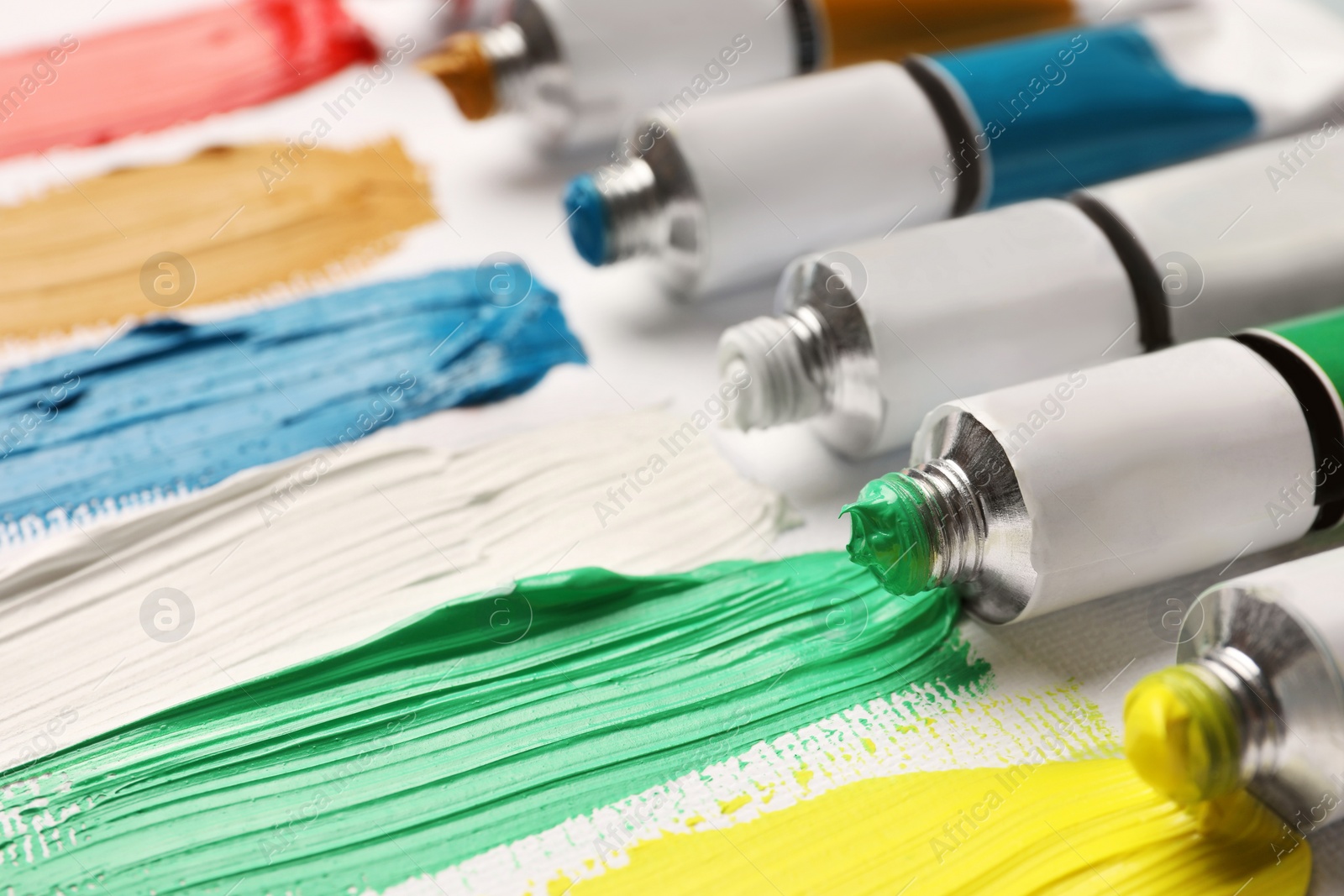 Photo of Tubes with oil paints and strokes on white canvas, closeup