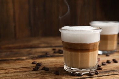 Photo of Delicious latte macchiato and coffee beans on wooden table, space for text