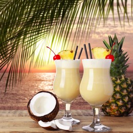 Image of Tasty Pina Colada cocktail on wooden table near ocean at sunset