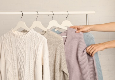 Photo of Woman choosing sweater on rack against brick wall