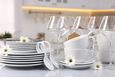 Photo of Set of clean dishware, glasses, cutlery and flowers on table in kitchen