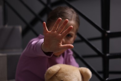 Photo of Child abuse. Girl with toy making stop gesture sitting on stairs, selective focus