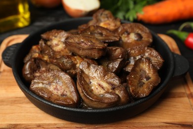 Photo of Frying pan with delicious kidneys on wooden board, closeup