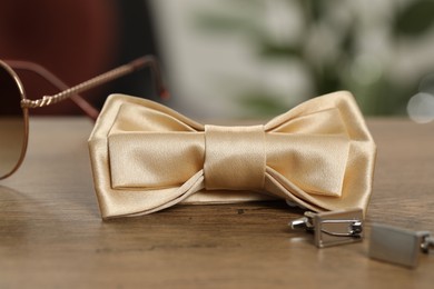 Photo of Stylish beige bow tie, sunglasses and cufflinks on wooden table, closeup