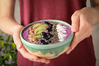 Woman holding bowl with tasty acai smoothie and fruits on blurred background, closeup