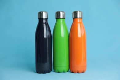 Photo of Stylish stainless thermo bottles on light blue background