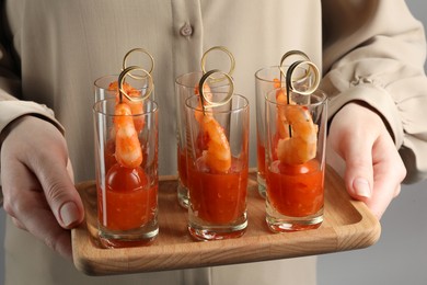Photo of Woman holding tasty canapes with shrimps, tomatoes and sauce in shot glasses on grey background, closeup
