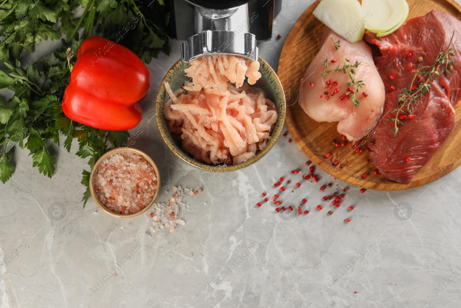 Photo of Electric meat grinder with chicken mince and products on grey marble table, flat lay. Space for text