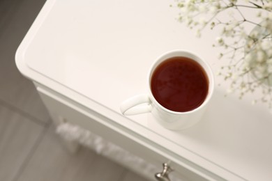 Photo of Ceramic mug with tea on white bedside table indoors, above view. Space for text