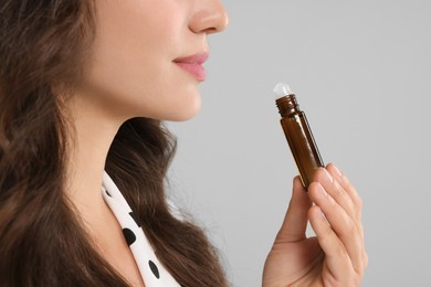 Woman with roller bottle of essential oil on light grey background, closeup