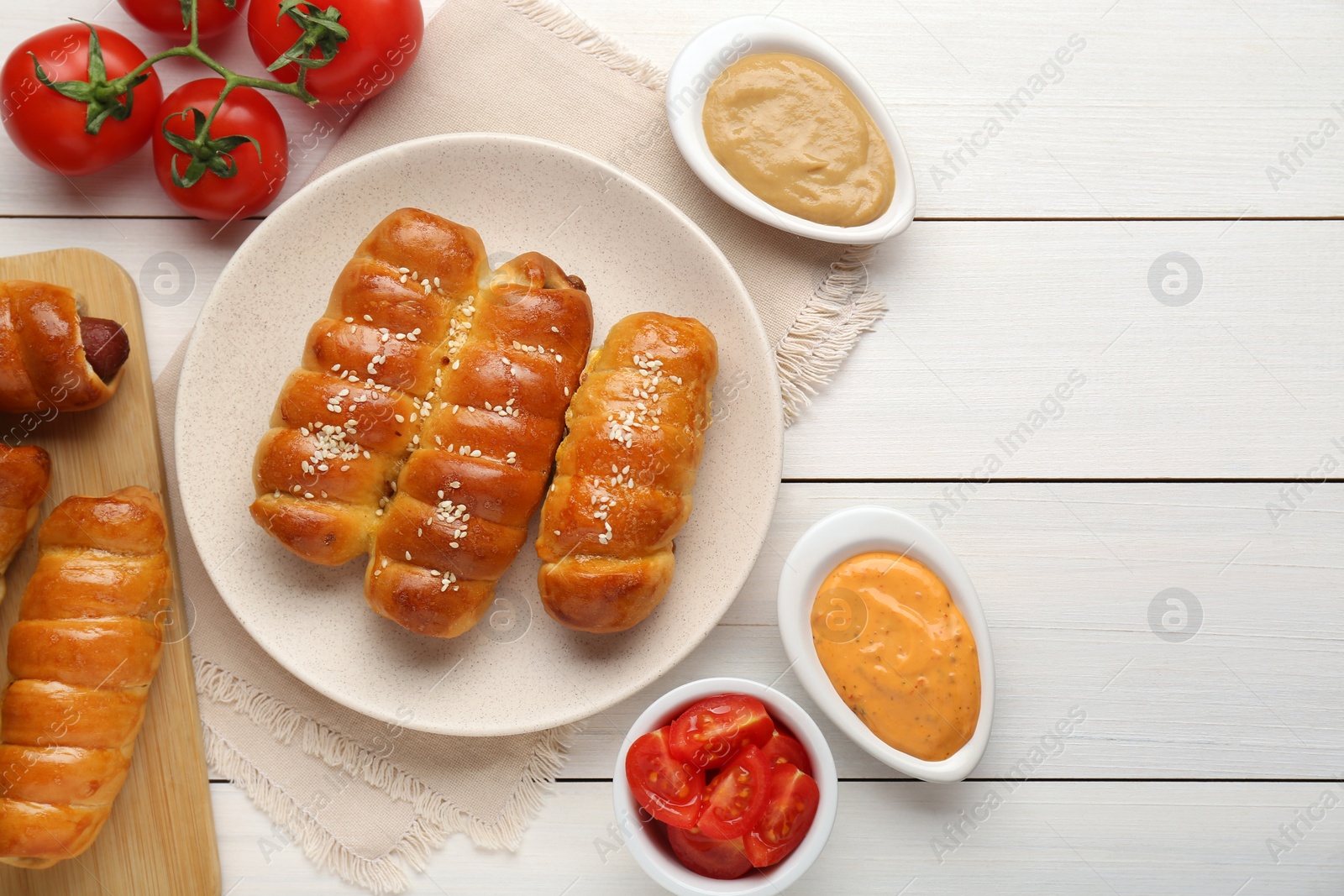 Photo of Delicious sausage rolls and ingredients on white wooden table, flat lay. Space for text