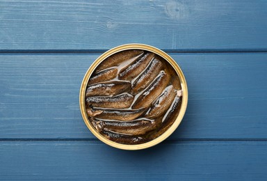 Photo of Open tin can of sprats on blue wooden table, top view