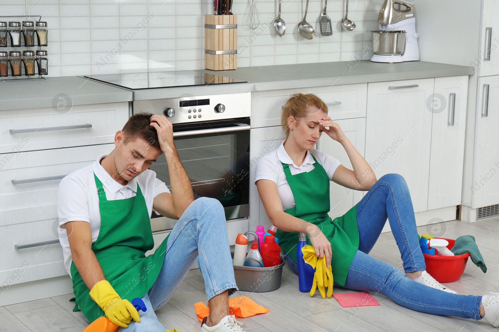 Photo of Exhausted janitors sitting on floor in kitchen. Cleaning service