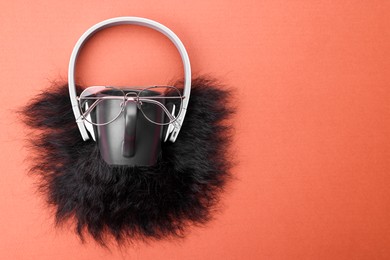 Photo of Man's face made of artificial beard, headphones and glasses on terracotta background, top view. Space for text