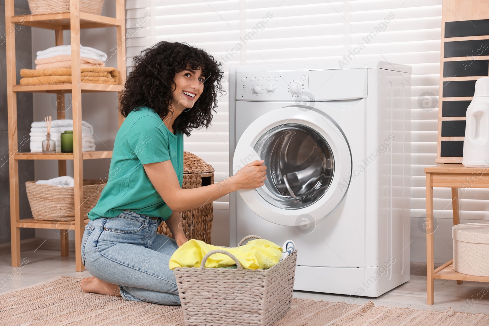 Photo of Happy woman with laundry near washing machine indoors