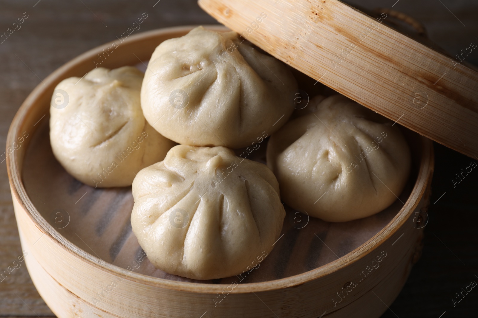 Photo of Delicious bao buns (baozi) in bamboo steamer on wooden table, closeup