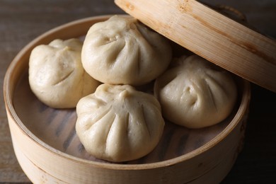 Photo of Delicious bao buns (baozi) in bamboo steamer on wooden table, closeup