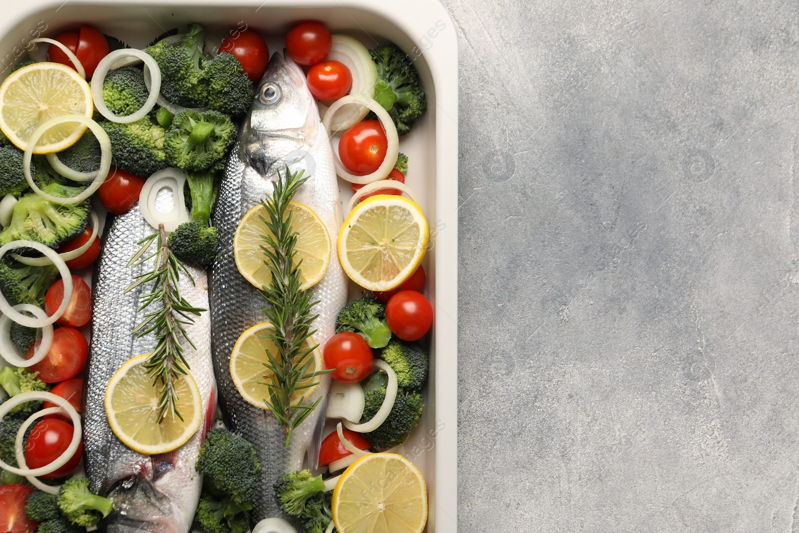 Photo of Raw fish with vegetables and lemon in baking dish on grey textured table, top view. Space for text