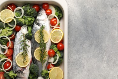 Photo of Raw fish with vegetables and lemon in baking dish on grey textured table, top view. Space for text