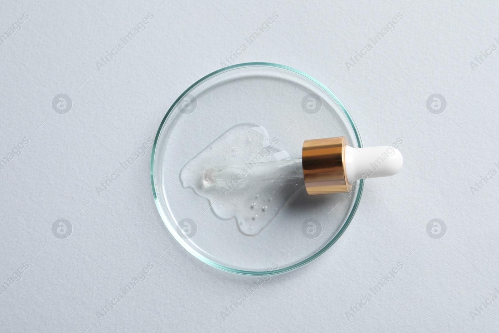 Photo of Petri dish with sample of cosmetic oil and pipette on white background, top view