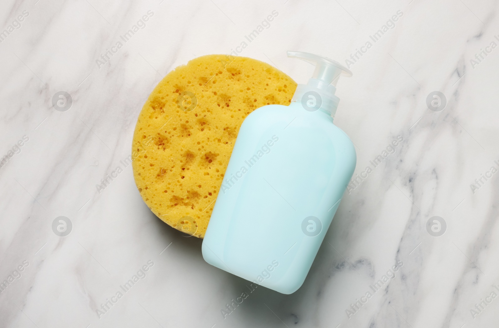 Photo of Dispenser of liquid soap and bath sponge on white marble table, flat lay