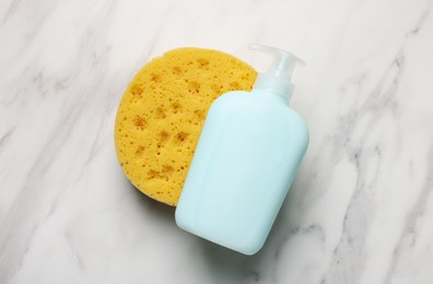 Dispenser of liquid soap and bath sponge on white marble table, flat lay