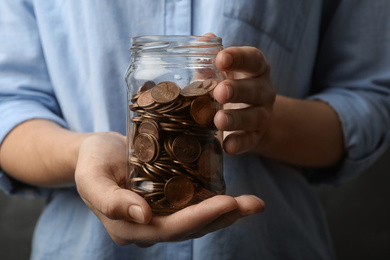 Woman holding glass jar with coins, closeup on hands