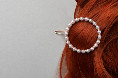 Photo of Elegant pearl clip and red hair strand on white background, top view. Space for text