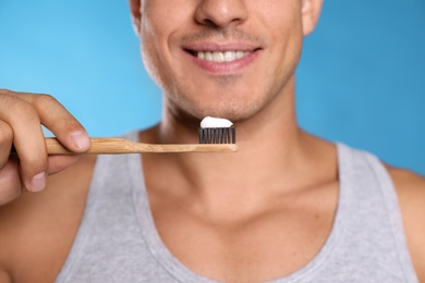 Photo of Man holding toothbrush with paste on blue background, closeup