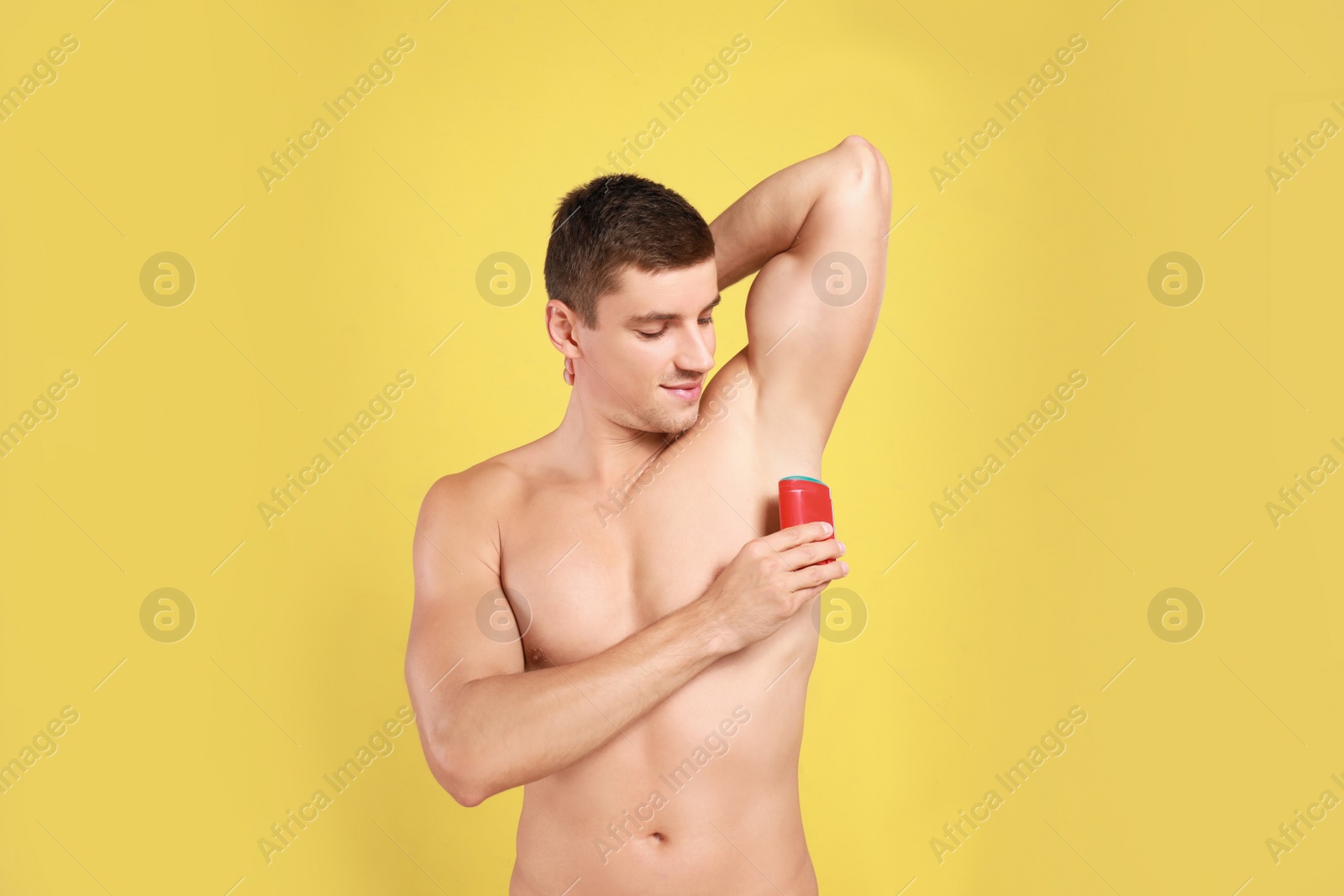 Photo of Young man applying deodorant to armpit on yellow background